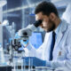 Scientist in white lab coat looking into microscope