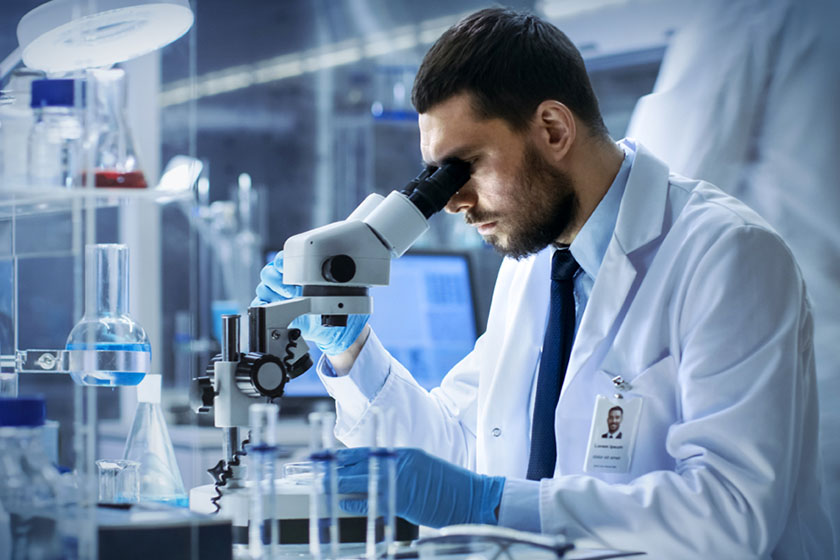 Scientist in white lab coat looking into microscope